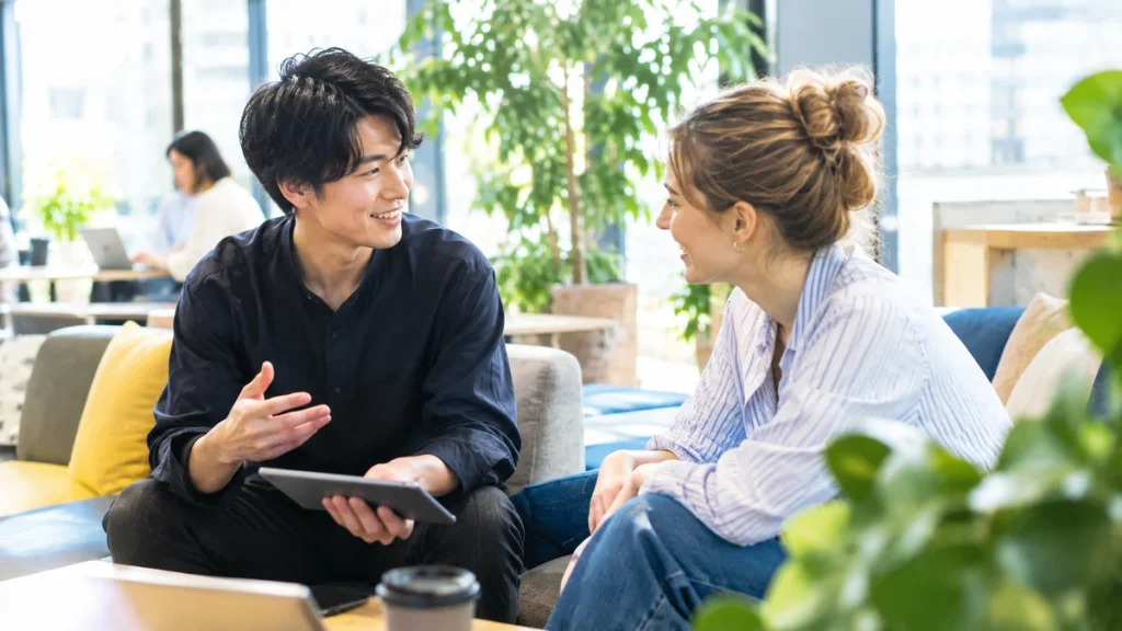 ラウンジのソファエリアで、笑顔でカジュアルに会話を交わす日本人男性と外国人女性のクリエイター。