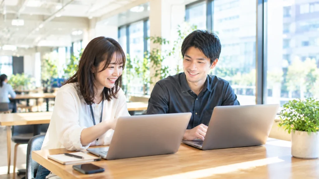 明るく清潔感のあるコワーキングスペースで、ノートパソコンを前に和やかに打ち合わせを行う日本人男女
